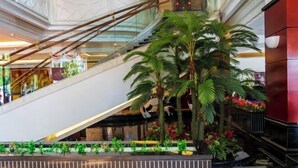Un centro comercial de varios niveles con una escalera mecánica de vidrio, palmeras y una pared de acento roja.