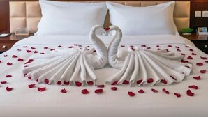 Una cama con una toalla dispuesta en forma de corazón y pétalos de rosa.
