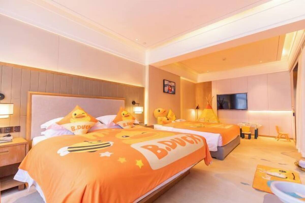 A hotel room with two beds, each with duck-themed bedding, a flat-screen TV, a desk with a chair, and a small table with a chair.