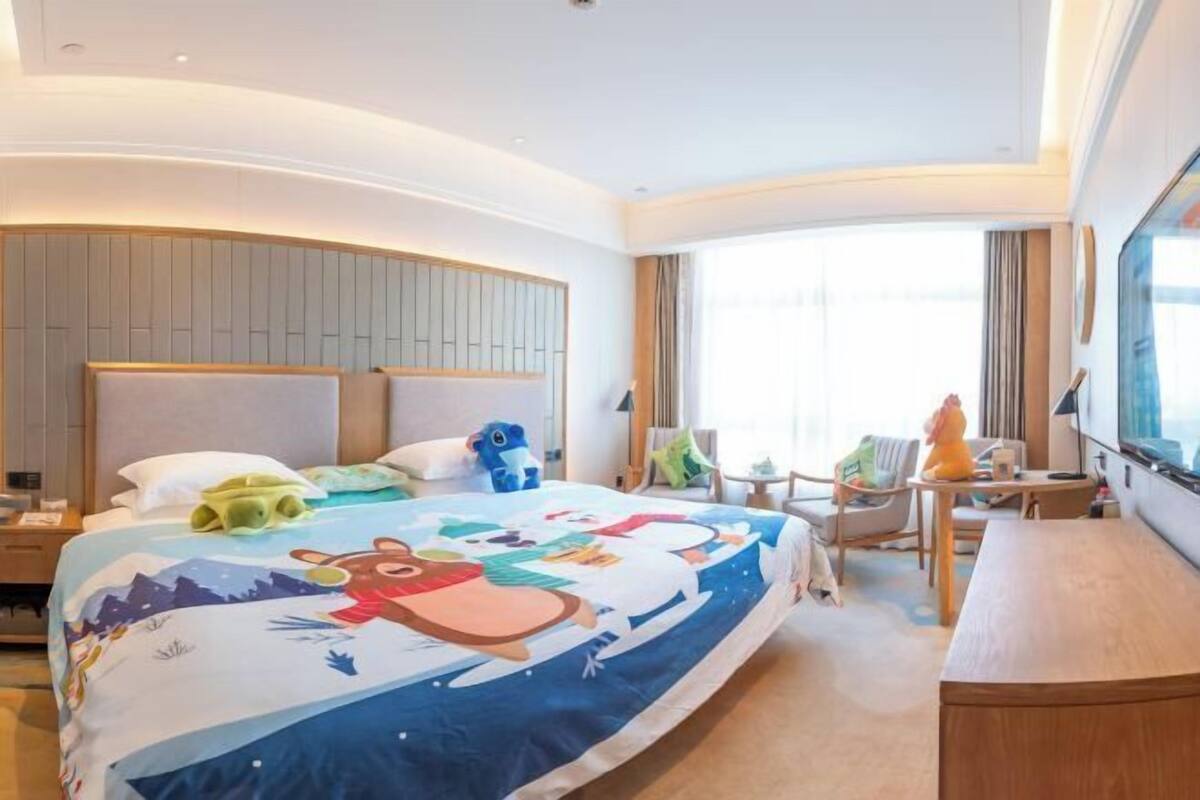 A hotel room with a large bed, a desk, a chair, a TV, and a window.