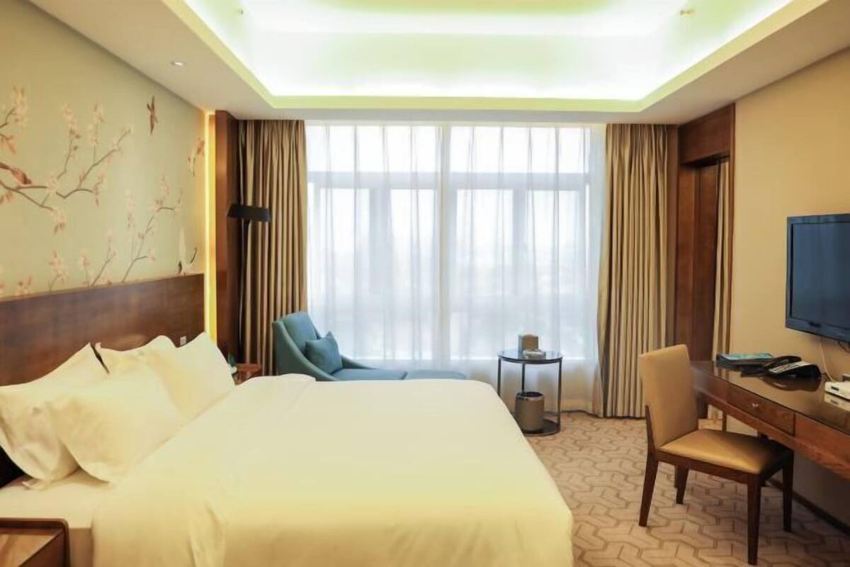 A hotel room with a large bed, a desk, a chair, a television, and a window with curtains.