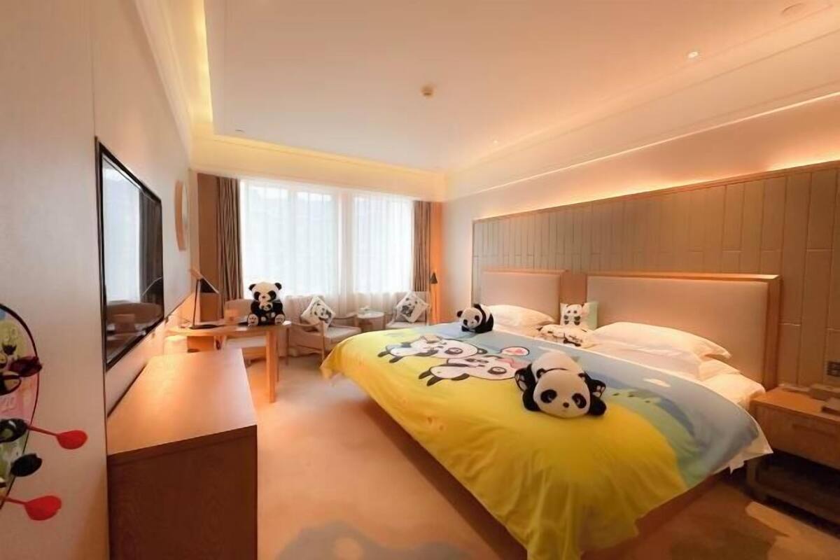 A hotel room with a bed, bedside tables, a TV, and a window with curtains.