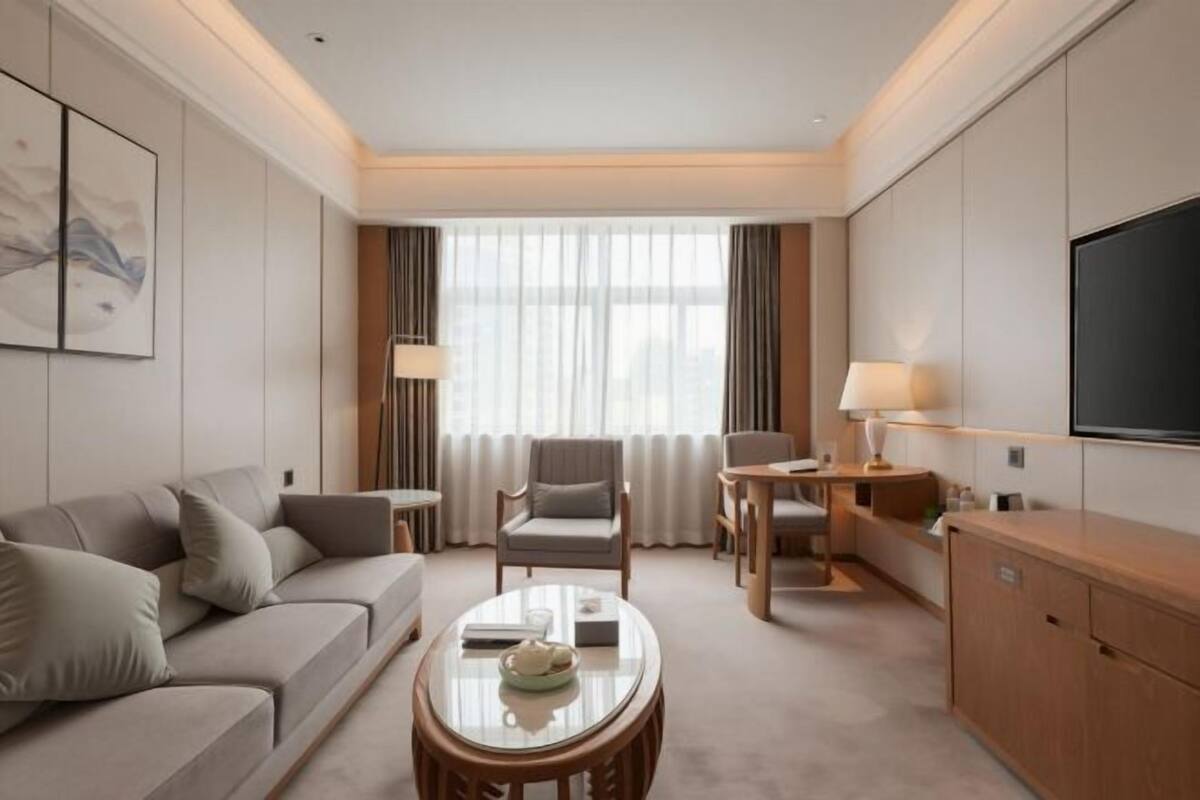 A hotel room with a sofa, a chair, a table, a TV, and a window with curtains.