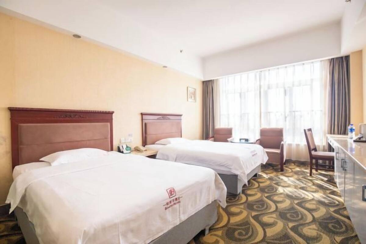 A hotel room with two beds, a desk, a chair, and a large window with curtains.