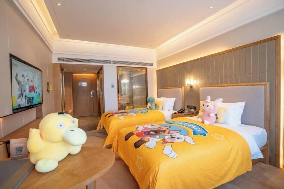 A hotel room with two beds, a large plush toy, and a TV on the wall.
