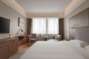 A hotel room with a large bed, a desk with a chair, a television, and a window with curtains.