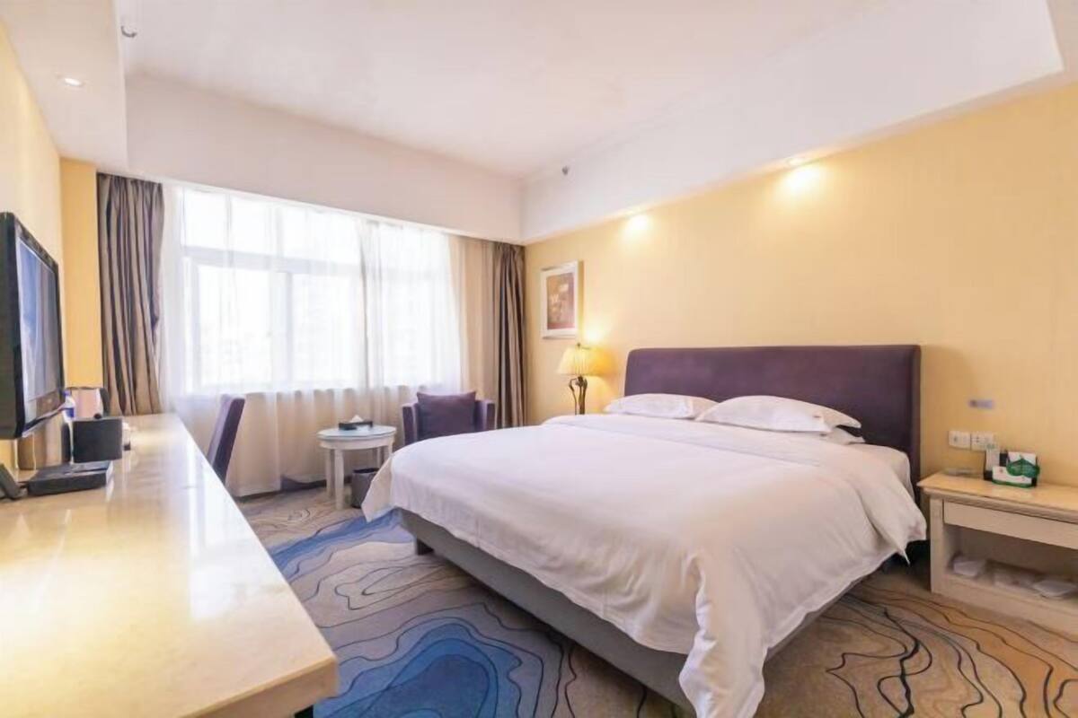 A hotel room with a bed, a desk, a TV, a lamp, and a window with curtains.