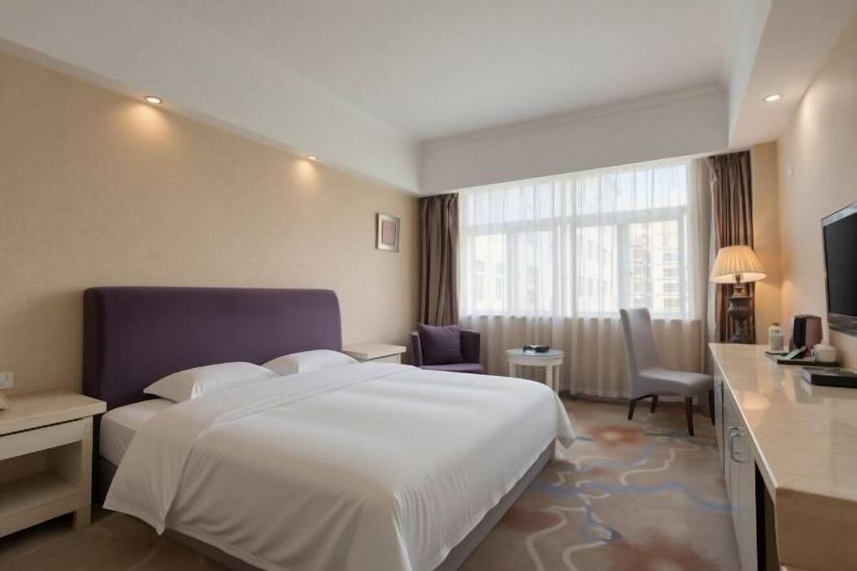 A hotel room with a bed, a desk, a chair, a TV, and a window with curtains.