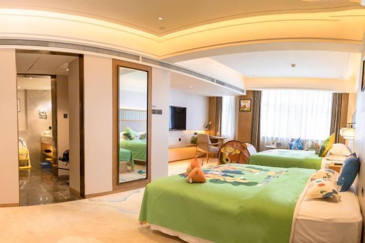 A hotel room with two beds, a sitting area, a TV, and a bathroom visible through an open door.