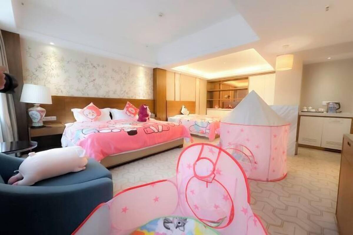 A hotel room with two beds, a desk, a chair, a small kitchenette, and a decorative tent.