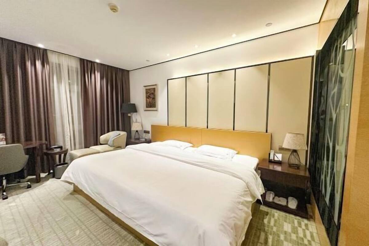 A hotel room with a large bed, a desk, a chair, a nightstand, and a mirror.