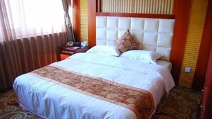 Une chambre d’hôtel avec un grand lit, une tête de lit, une table de chevet et une fenêtre avec des rideaux.
