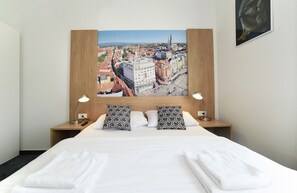 A hotel room with a large bed, two bedside lamps, patterned pillows, and a cityscape painting on the headboard. - Hotel Orient Zagreb (Zagreb)
