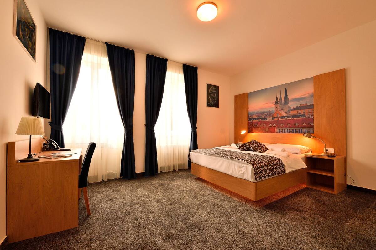 Habitación de hotel con cama, escritorio, silla y un cuadro de un paisaje urbano.