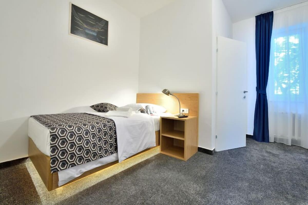 Habitación de hotel con cama, mesita de noche, lámpara y puerta que da a un balcón.