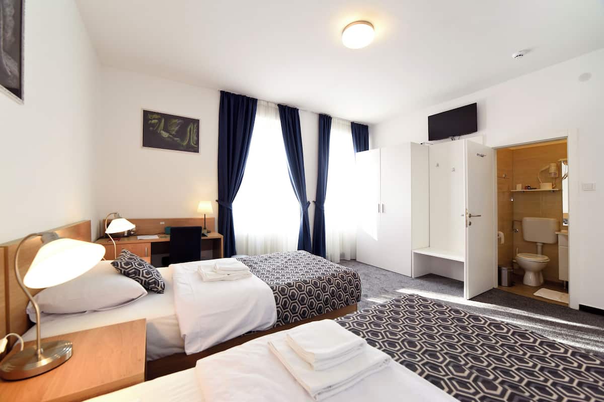 Habitación de hotel con dos camas, un escritorio, una silla, una lámpara, televisión y baño.