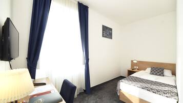 Een hotelkamer met een bed, een bureau met lamp, een stoel, een televisie en een raam met gordijnen.