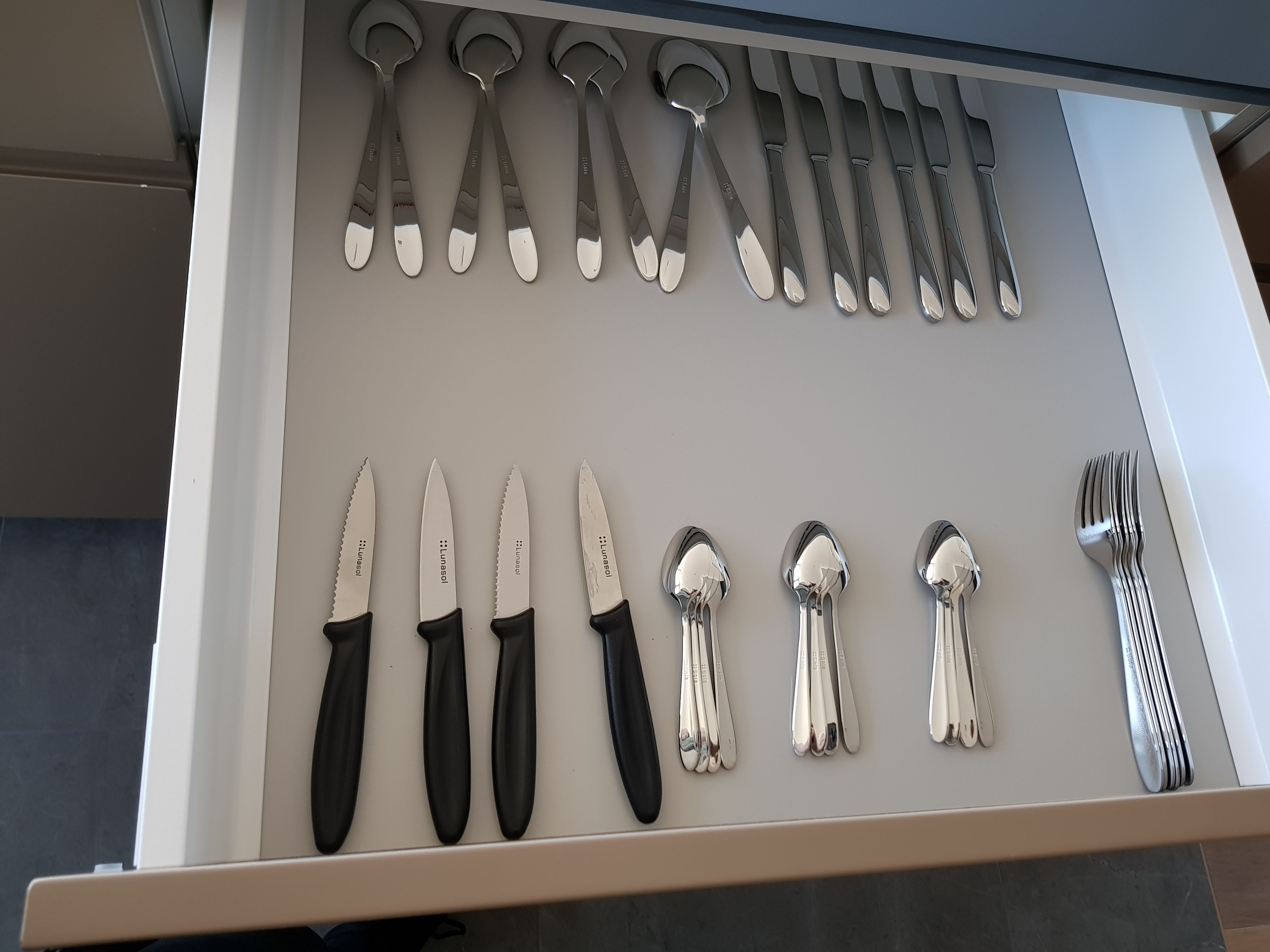 A drawer containing various kitchen utensils including spoons, forks, and knives.