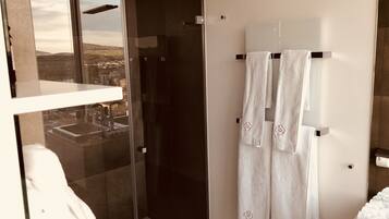 A modern bathroom with a glass shower enclosure, a white towel rack with towels, and a small white table with a soap dispenser.
