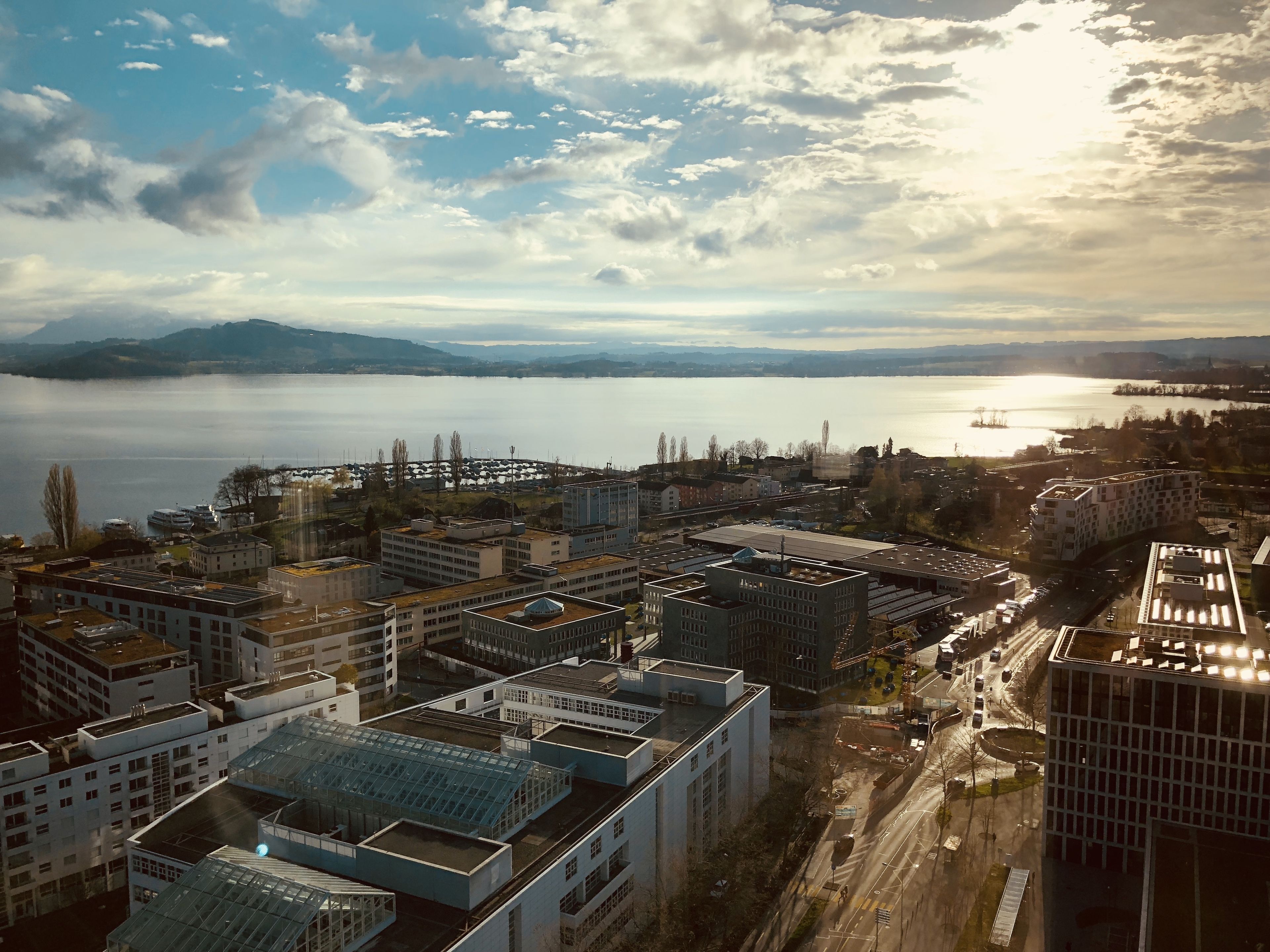 Vista aérea de una ciudad con edificios modernos, una masa de agua extensa y montañas distantes.