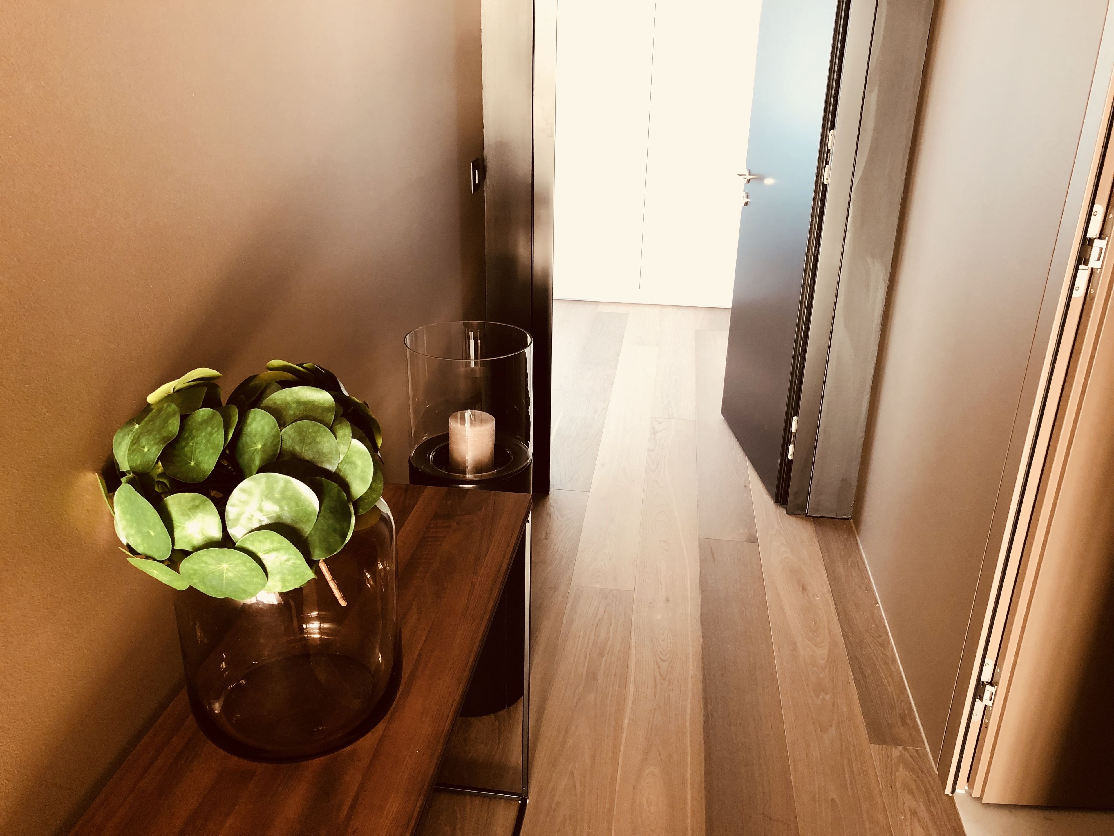 A hallway with a wooden bench, a potted plant, a glass candle holder, and a door.