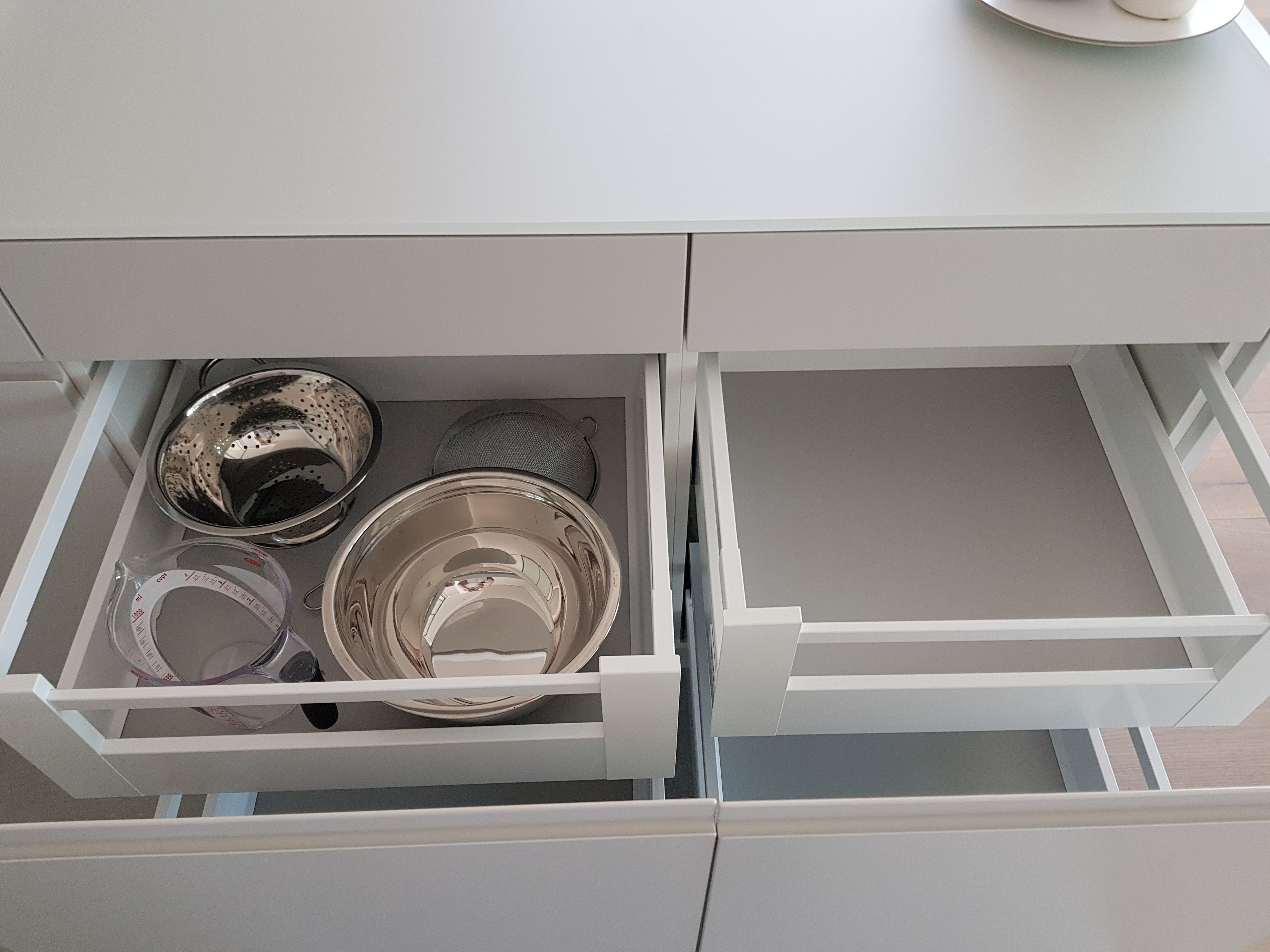 En låda med diverse köksredskap, inklusive en durkslag, sil och måttsatser.