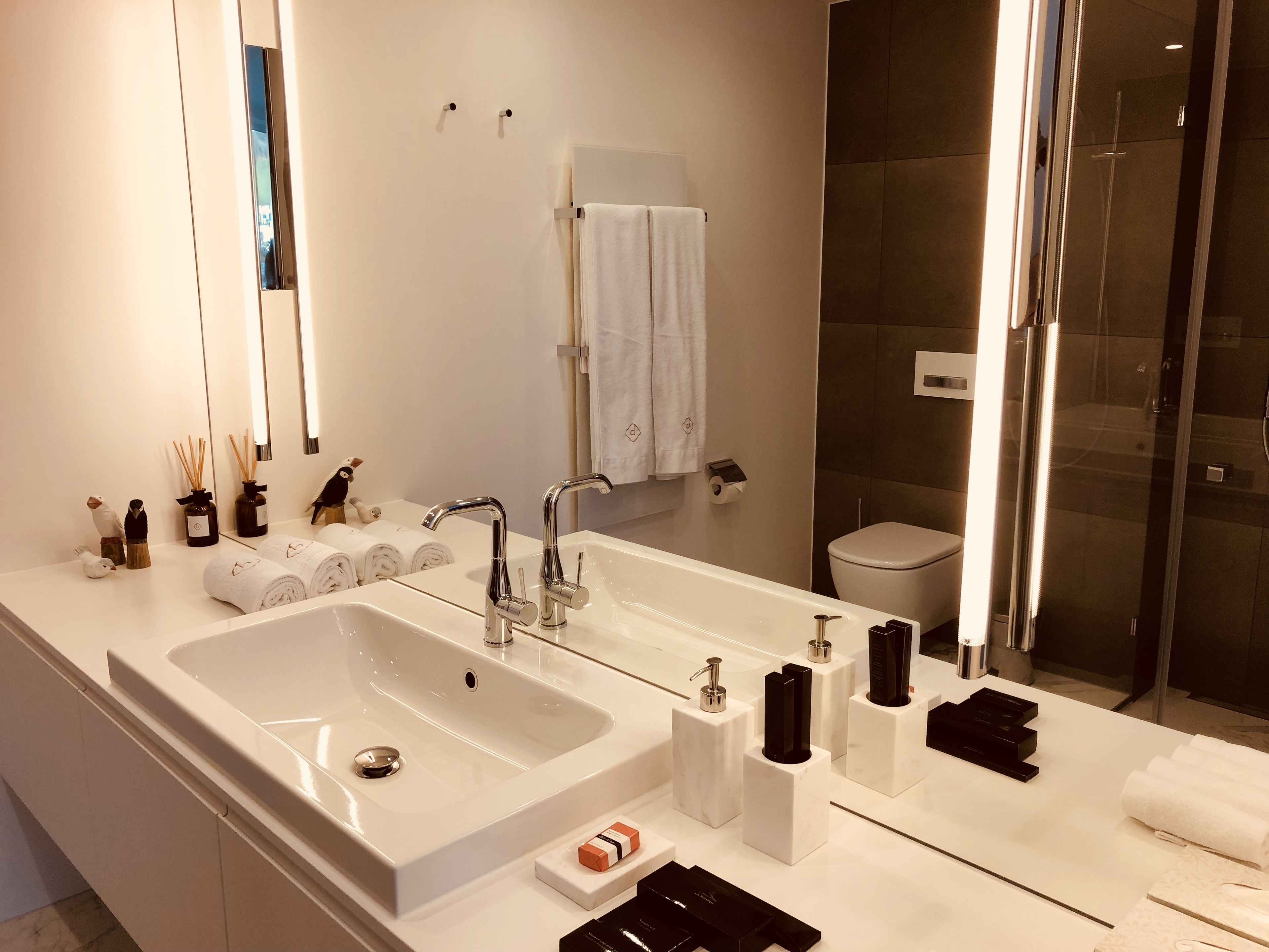Un baño moderno con un lavamanos grande de color blanco, dos grifos, un espejo y una cabina de ducha de vidrio.