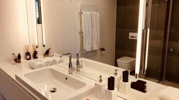 Un baño moderno con un lavamanos grande de color blanco, dos grifos, un espejo y una cabina de ducha de vidrio.