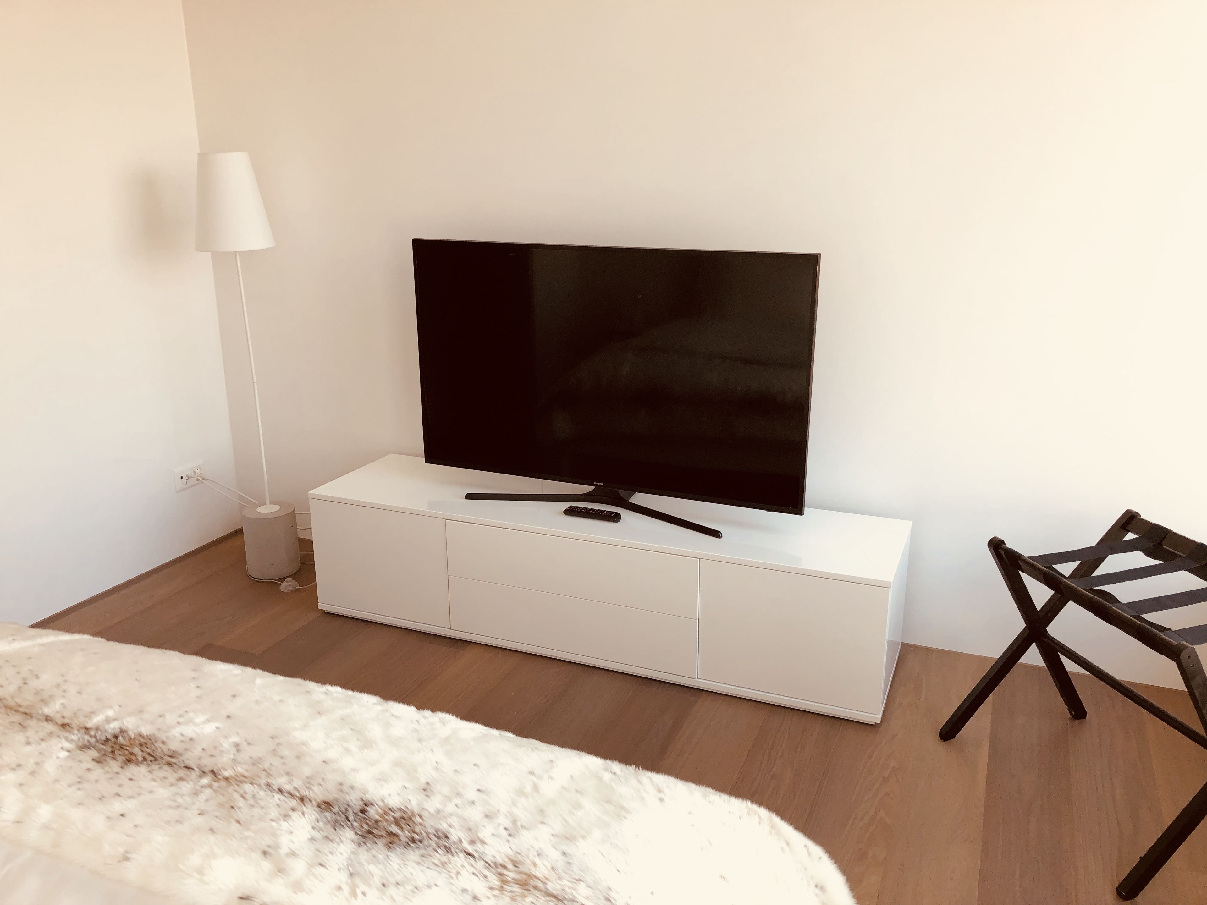 A modern room with a flat-screen TV on a white cabinet, a lamp, and a wooden floor.
