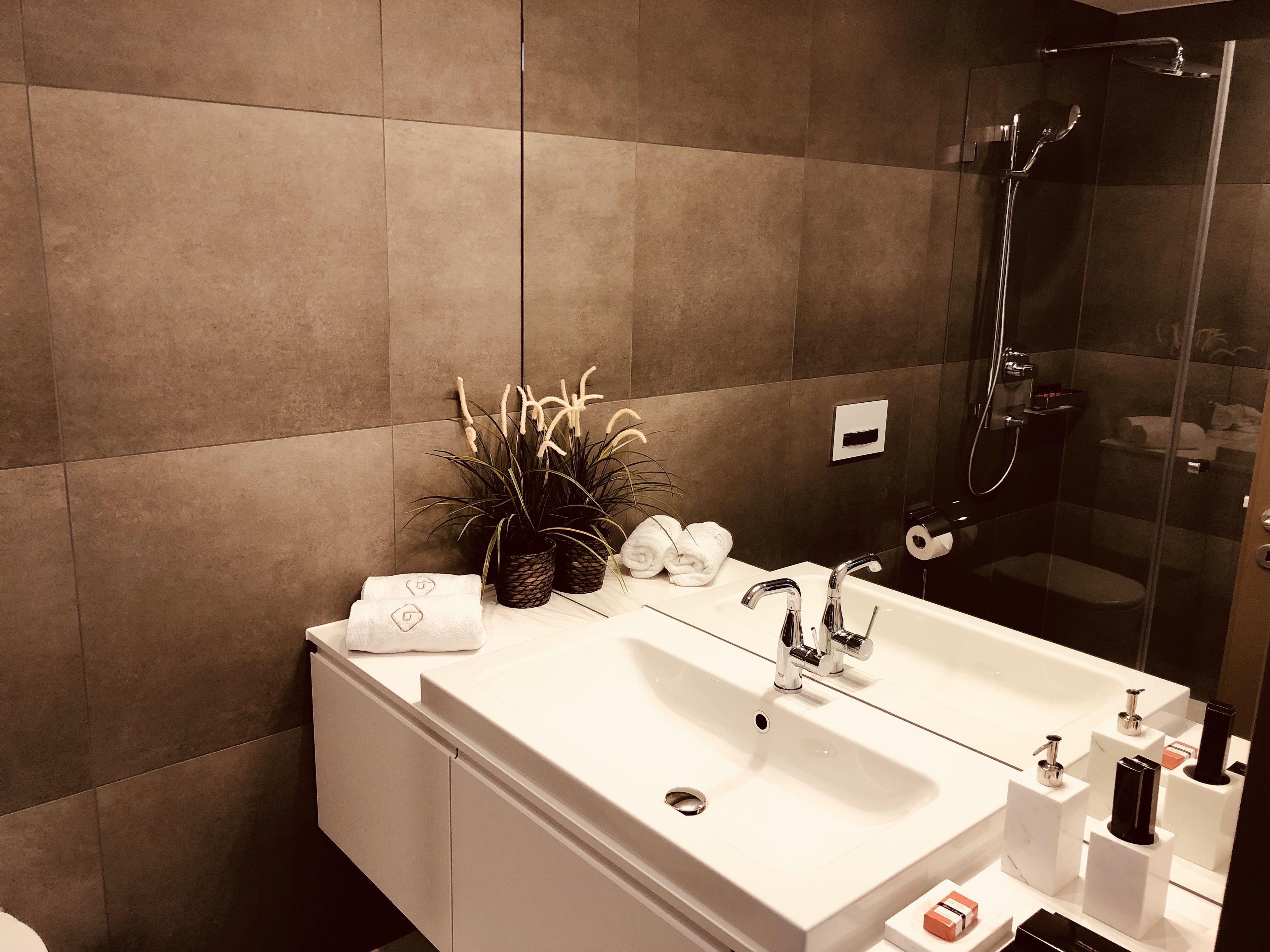 Een moderne badkamer met een groot wastafelmeubel, een douchecabine van glas en een plant in pot.