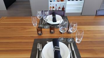 A dining table set with wine glasses, water glasses, and cutlery, with a wine refrigerator in the background.