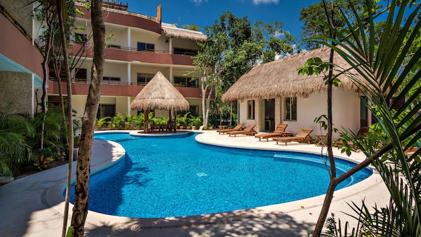 A resort pool area with a clear blue pool, lounge chairs, and thatched-roof structures. - El Cielo 1BRM Penthouse private roof sleeps 3 (Tulum)