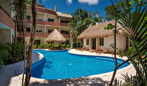 A resort pool area with a clear blue pool, lounge chairs, and thatched-roof structures. - El Cielo 1BRM Penthouse private roof sleeps 3 (Tulum)