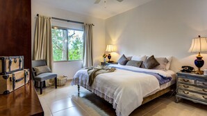 A bedroom with a large bed, two bedside tables with lamps, a chair, a wooden chest, and a window with curtains. - El Cielo 1BRM Penthouse private roof sleeps 3 (Tulum)