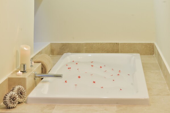 A bathtub with rose petals floating in the water, a candle, and decorative flowers on the side.