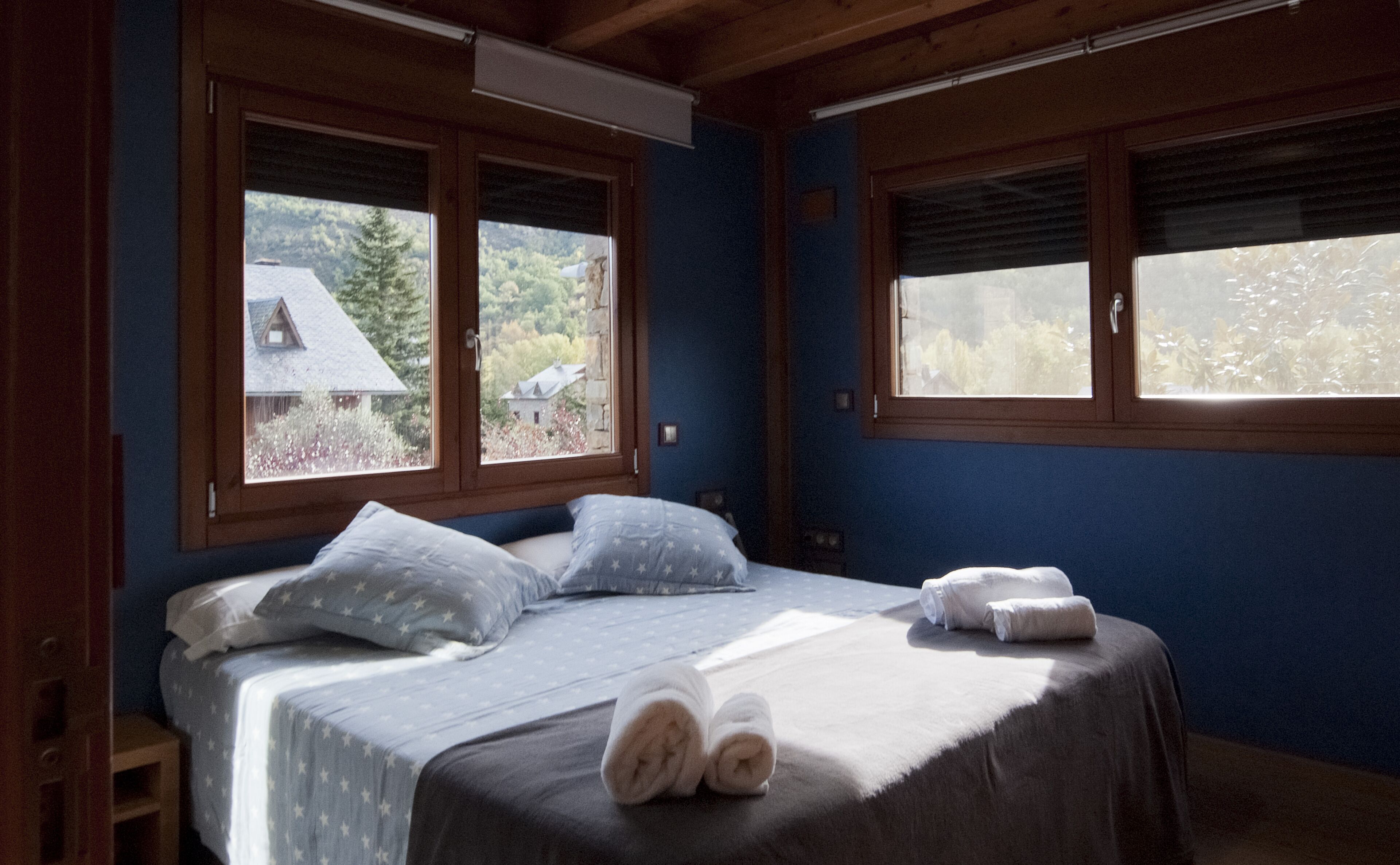 A bedroom with a bed, two windows, and a view of houses and trees.