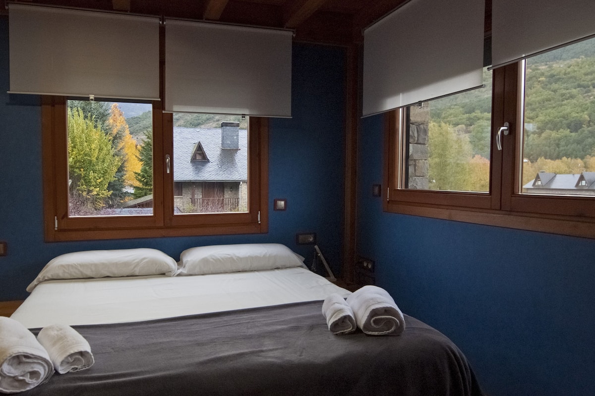 A bedroom with a bed, two windows, and a view of a house and trees.