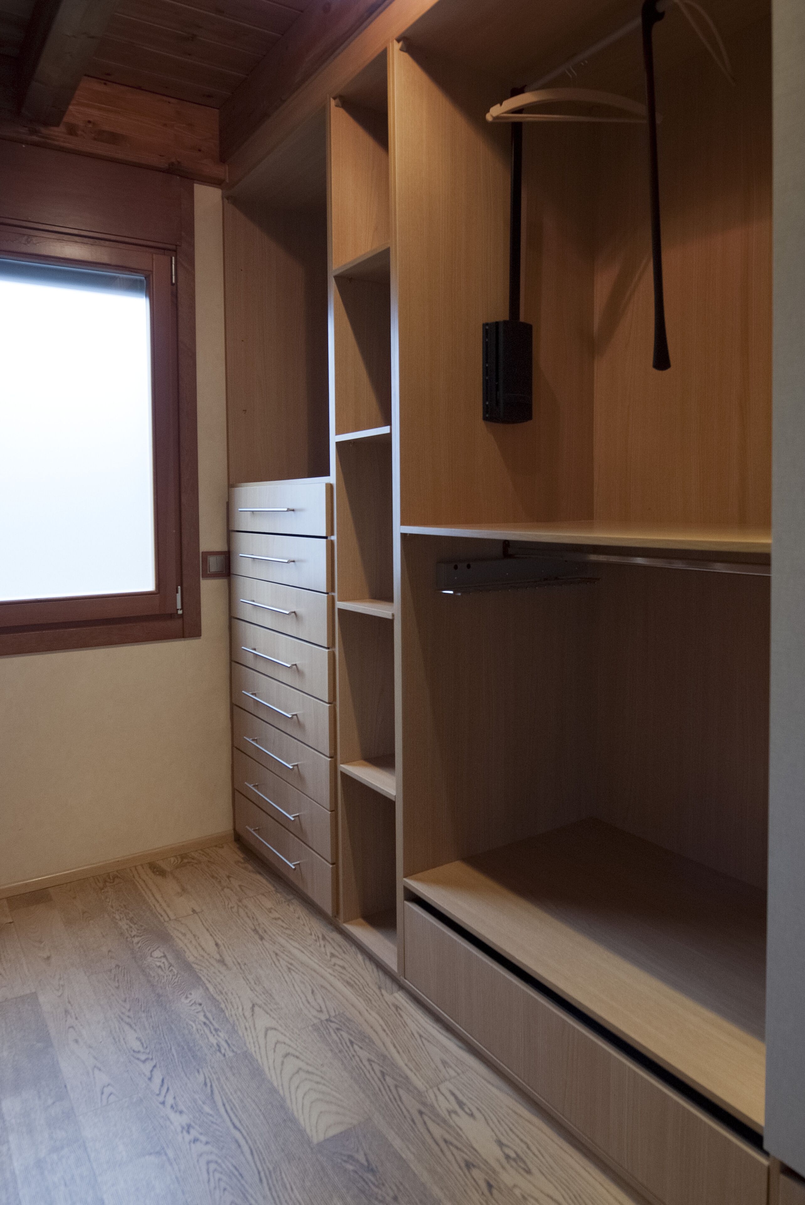 Een kamer met een houten garderobe, een raam en een plankunit.