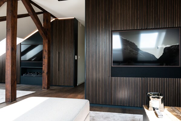 Een moderne kamer met een grote televisie aan de muur, houten balken en een stenen openhaard.