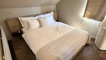Um quarto com cama, mesas de cabeceira e uma janela.
