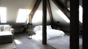 A bedroom with a sloped ceiling, skylights, a bed, a sofa, and a bedside table.