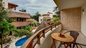 Un balcón con una mesa y sillas de madera, con vistas a una piscina y un jardín tropical.