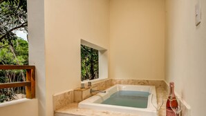 Un baño con bañera, una ventana que da a zonas verdes y una botella de vino sobre la encimera.