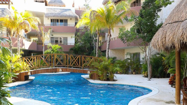 Una piscina rodeada de edificios con techo de paja, palmeras y un puente de madera.