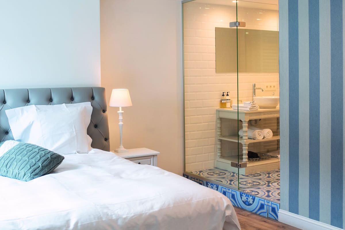 Une chambre à coucher avec un lit, une lampe de chevet et une salle de bain visible à travers une cloison en verre.