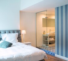 A bedroom with a bed, bedside lamp, and a bathroom visible through a glass partition.