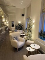 A modern interior with plush armchairs, a tall Christmas tree, and a bar area with stools.