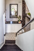 A staircase with a black and white patterned floor leading to a bathroom with a black marble countertop and a white vanity.