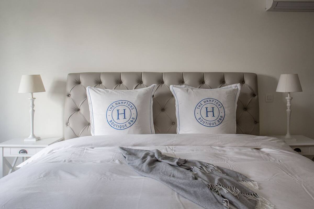 Un lit bien fait, avec deux oreillers ornés d’un logo, une tête de lit capitonnée et des lampes de chevet de chaque côté.
