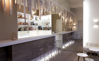 A modern bar area with a wooden counter, shelves with bottles, and clear stools.